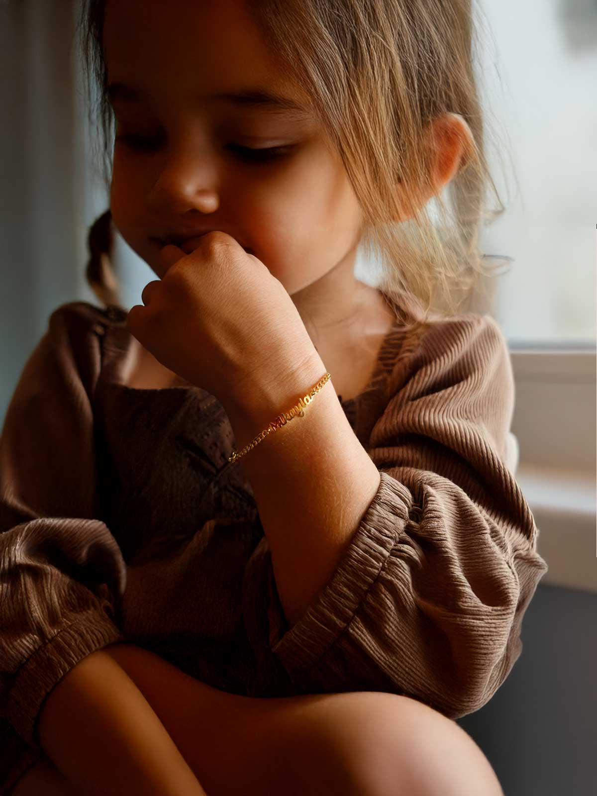 a little girl sitting on a window sill holding her hand to her face