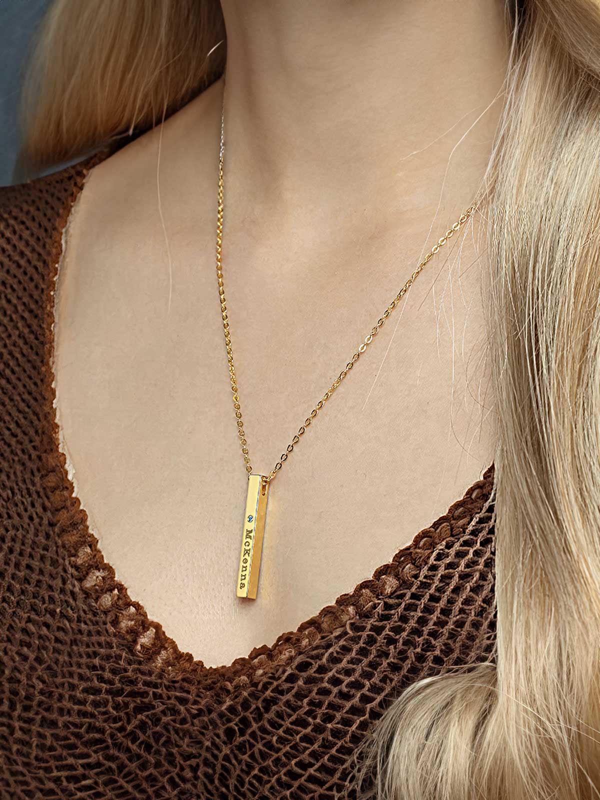 a woman wearing a gold necklace with a bar on it